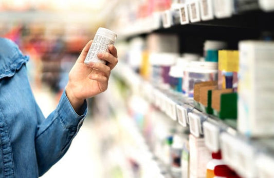 Person examining a supplement bottle in a health store aisle filled with various products.
