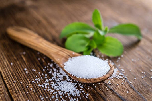 En sked med stevia och gröna blad på en träyta, som visar ett naturligt sockeralternativ.