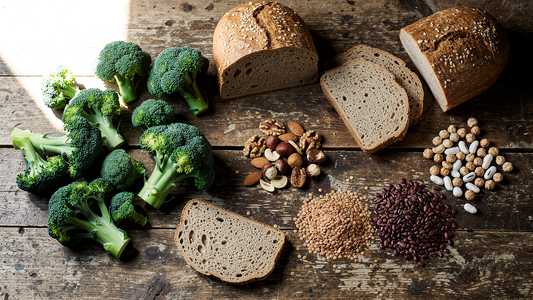 Kromrika livsmedel som broccoli, fullkornsbröd, nötter och baljväxter på ett träbord