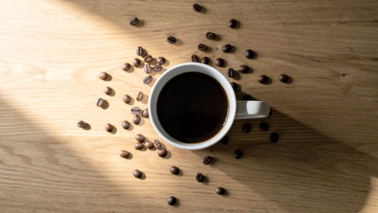 En nybryggd kopp svart kaffe på ett träbord med spridda kaffebönor i morgonljus