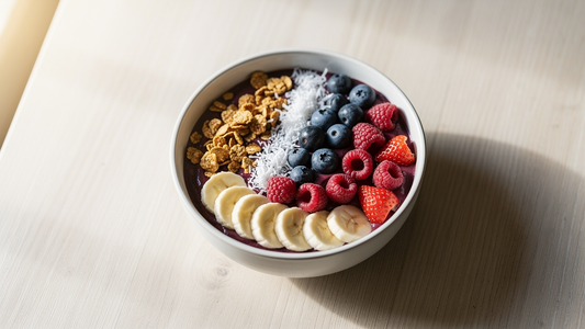 Acai-bowl toppad med banan, granola och färska bär i en skål på ett ljust träbord