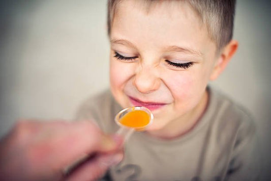 Young boy grimacing while taking liquid vitamin supplement from a spoon, showcasing healthy habits.