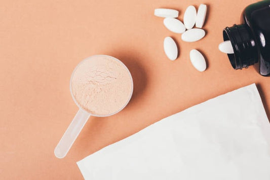 BCAA supplement powder in a scoop with white tablets and a black container on a beige background.