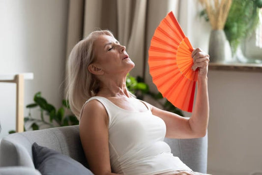 Older woman using a fan to cool down, representing menopause discomfort and seeking relief.