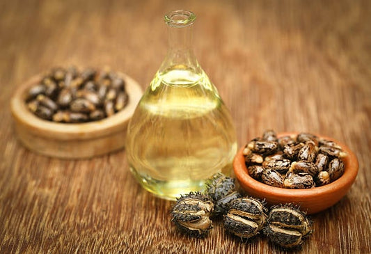 Castor oil in a glass bottle with castor seeds in bowls on a wooden surface.