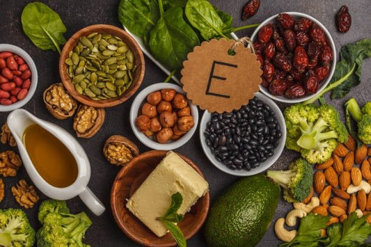 Samling av livsmedel rika på E-vitamin, inkluderande nötter, frön, avokado och olja på en mörk bakgrund.