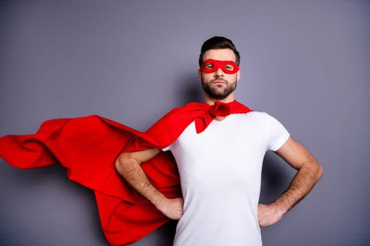 Man wearing a red cape and mask, posing confidently against a gray background.