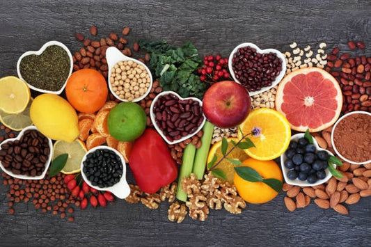 A colorful assortment of fruits, vegetables, nuts, and spices displayed in heart-shaped bowls on a dark background.