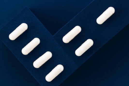 Vita kapslar av 5-HTP på en mörkblå yta, representerande naturlig hälsa och välmående.