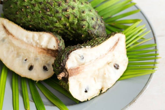Halved graviola fruit showing creamy flesh and seeds, nestled on green leaves.
