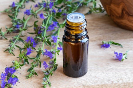 Flask av hyssopolja omgiven av blommor på en trätablett.