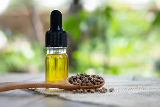 Flacon with hemp seed oil beside hemp seeds on a wooden spoon, emphasizing health benefits.
