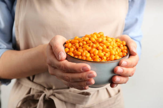 Person holding a bowl filled with fresh sea buckthorn berries.