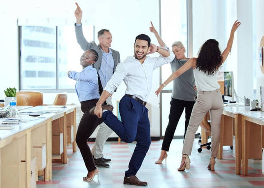 En grupp människor i kontorsmiljö som dansar och uttrycker glädje för att öka energin.