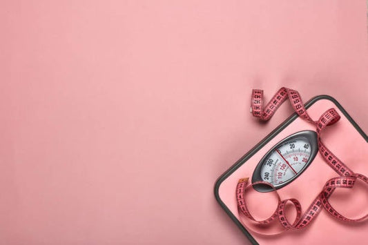 Viktvåg på rosa bakgrund med måttband, symboliserar viktminskning och hälsa.