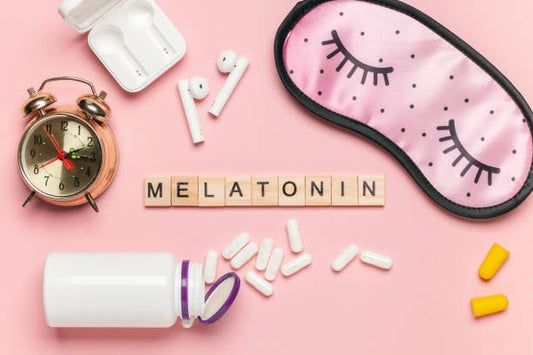 Flat lay of melatonin supplements, alarm clock, sleep mask, and earplugs on a pink background.
