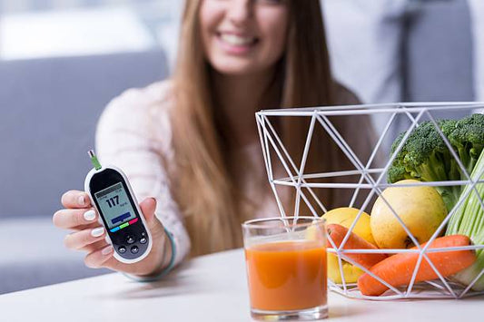Woman measuring blood sugar with a glucometer beside a basket of fresh fruits and vegetables.