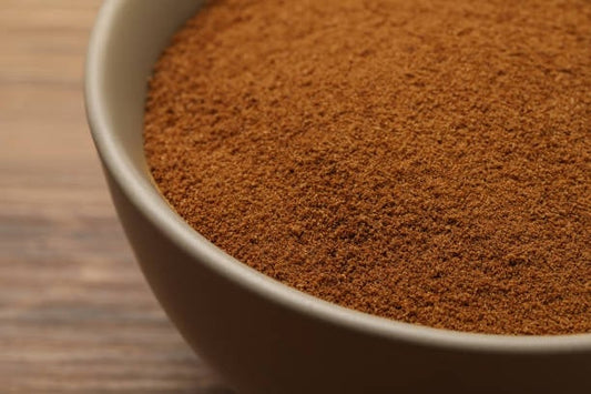 A close-up view of a bowl filled with brown inulin powder on a wooden surface.