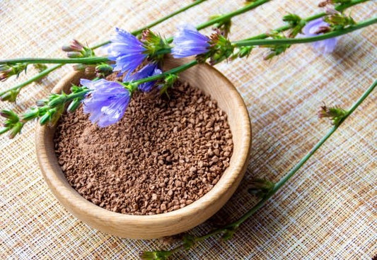 En skål med inulinpulver omgiven av blå blommor på en texturerad bakgrund.
