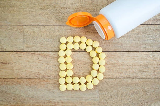 Gula D-vitamintabletter formade som bokstaven D, med en flaskan ovanpå träyta.