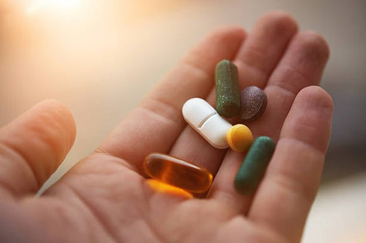 A hand holding various vitamin and supplement capsules, including D-vitamin and magnesium.