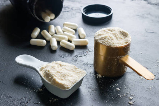 Kasein och vassleproteinpulver i måttkoppar med kosttillskott i bakgrunden.