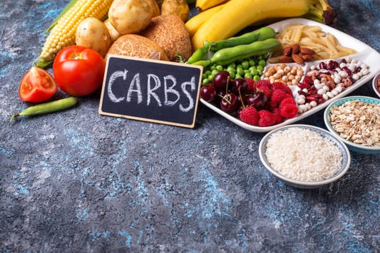 Colorful assortment of healthy carbohydrates including fruits, vegetables, and grains with a chalkboard sign labeled 'CARBS'.