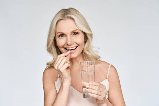 Woman smiling while taking a collagen tablet with a glass of water