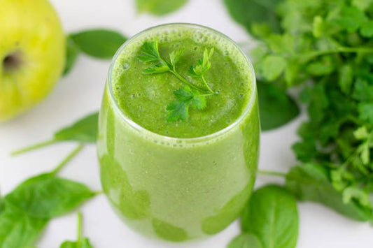 Grön smoothie med persilja, spenat och äpple, omgiven av färska örter.