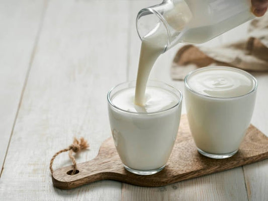 Fräsch syrad mjölk hälls från en flaska i två glas på ett träskärbräda.