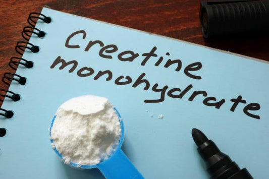 Blue scoop of creatine monohydrate powder on a notepad with handwritten label.