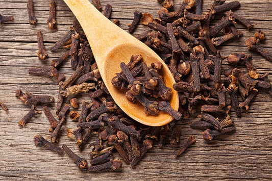 A wooden spoon filled with dried cloves on a rustic wooden surface.