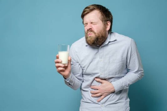 Man with a pained expression holding a glass of milk, showing discomfort likely due to lactose intolerance.
