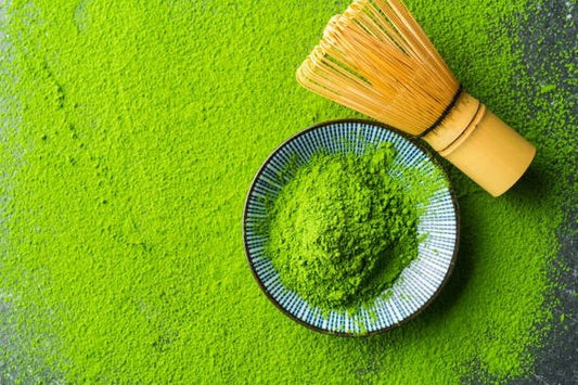 Matcha powder in a bowl with a bamboo whisk on a green textured surface.