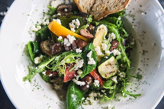 Fresh Mediterranean salad with colorful vegetables, olives, and feta cheese, served with bread.