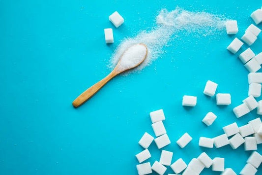 Wooden spoon with sugar granules and sugar cubes on a blue background, representing discussions about sugar misconceptions.