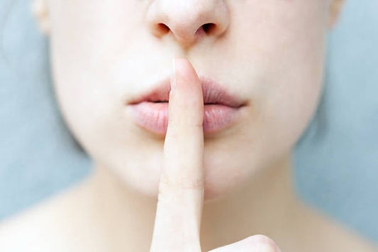 Woman's face making a shushing gesture with a finger on her lips, promoting silence and tranquility.