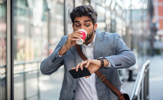 Man in a suit drinking coffee while checking his phone, looking busy and on-the-go.