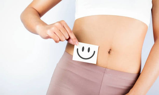 Woman holding a smiley face sign over her stomach, symbolizing gut health and positivity.