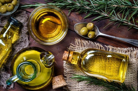 Various bottles of olive oil and olives on a rustic wooden table with rosemary.