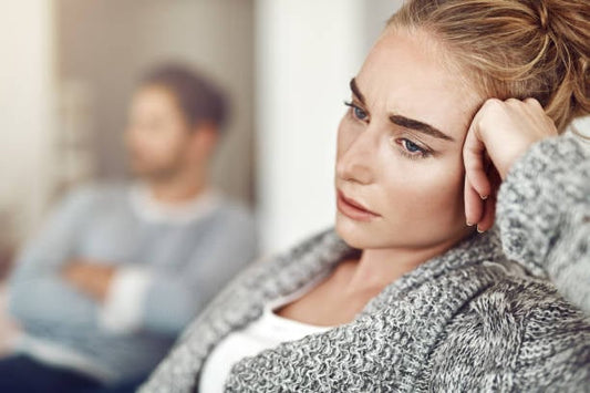 En kvinna ser bekymrad ut och funderar över sina känslor, medan mannen bakom verkar distanserad.