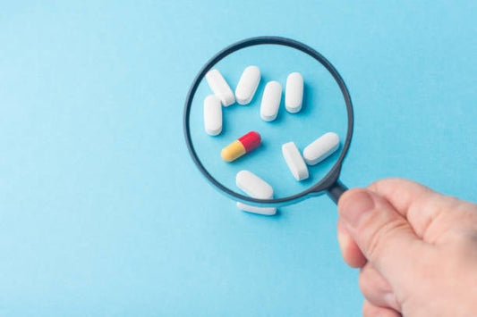 Hand holding a magnifying glass over various vitamins and supplements on a blue background.