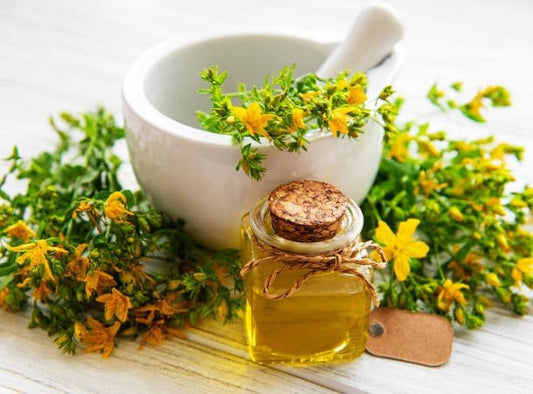 Glass jar of St. John’s wort oil with yellow flowers and a mortar and pestle.
