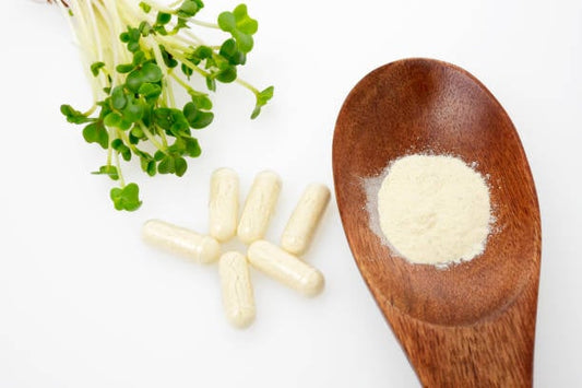Broccoli sprouts, dietary supplements in capsules, and sulforaphane powder on a wooden spoon.