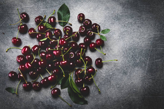Luscious black cherries with green leaves on a dark stone surface, highlighting their rich color and freshness.
