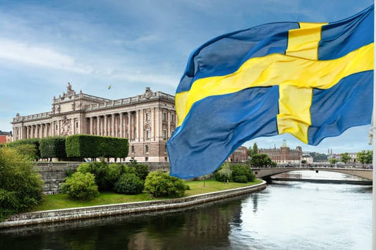 Swedish flag fluttering in front of a historic building by a river in Sweden.