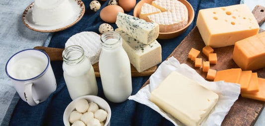Diverse kalciumrika livsmedel inklusive mjölk, ost, ägg och yoghurt på ett bord.