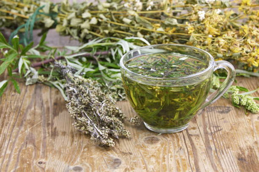 A clear glass cup filled with herbal tea made from various dried herbs, resting on a wooden surface.