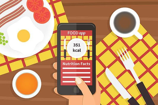 En hand håller en smartphone som visar 351 kcal från en matapp, med en frukosttallrik i bakgrunden.
