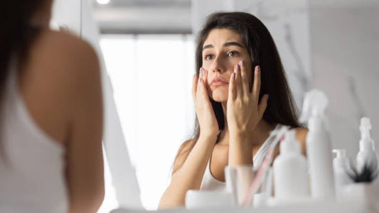 Woman applying skincare products while looking in the mirror at home.